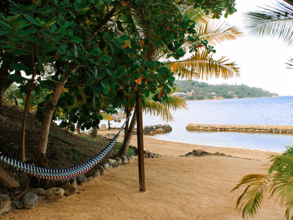 An empty hammock lays in the shade overlooking the sandy beach of Roatan at Marble Hill Resort